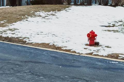 Bright red fire hydrant stands out on snowy lawn beside asphalt road on a c.. Stock Photos