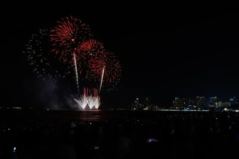 Bright Red Fireworks Exploding Over Coastal City Skyline Night Wide Shot Stock Photos
