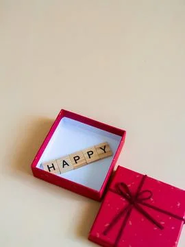Bright red gift box filled with wooden letters that spell out the word happ.. Stock Photos