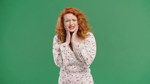 Bright red-haired woman with tooth pain, green studio. Toothache, dental problem Stock Footage 312837553
