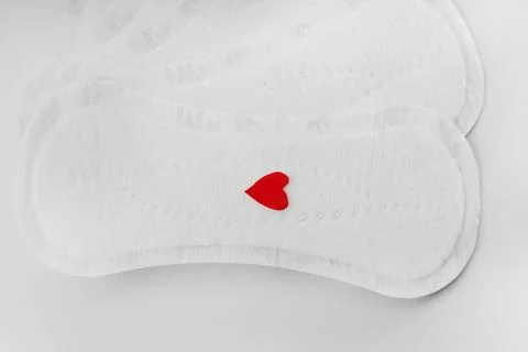 Bright red heart on a stack of new white feminine pads on a light background. Stock Photos