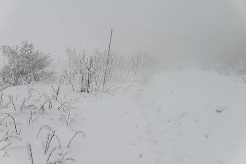 A bright red mountain trail marker stands in deep snow and thick fog, guidi.. Stock Photos