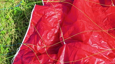 Bright red paraglider wing lying on meadow grass, with tangled suspension Video stock 337505817
