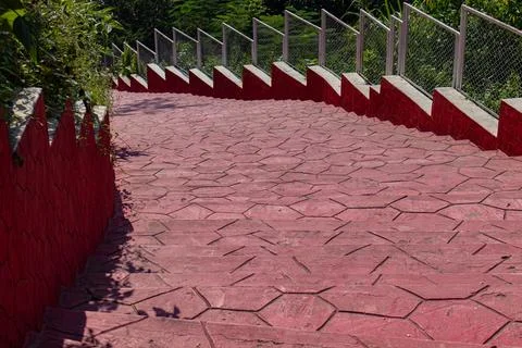 Bright red patterned concrete pathway with railings leading downhill at Drea Stock Photos