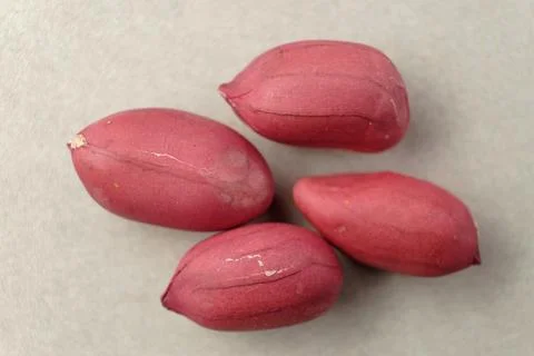 Bright red peanuts resting on a smooth grey surface under soft morning light Foto stock