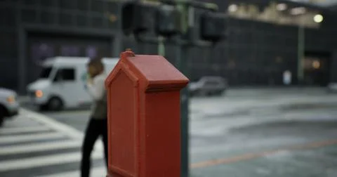 Bright red post box stands prominently at a city intersection during the day Illustrazione stock