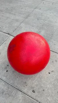 Bright red spherical object placed on concrete pavement in an urban setting.. Stock Photos