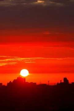 A bright red sun disk rises in the early morning over the silhouettes of city Stock Photos