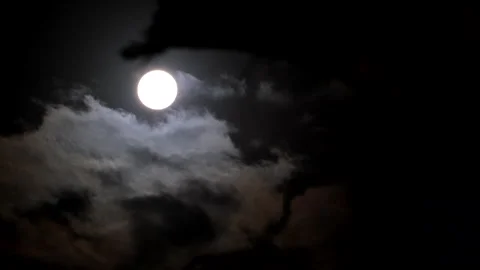 Bright round orb of full moon in dark night sky as clouds ominously pass by 動画素材 320432971