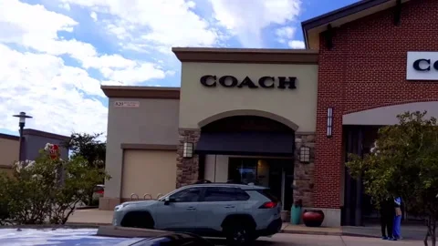Bright sky, slow-motion pan outside front of Coach store in outdoor outlet mall 動画素材 165429730