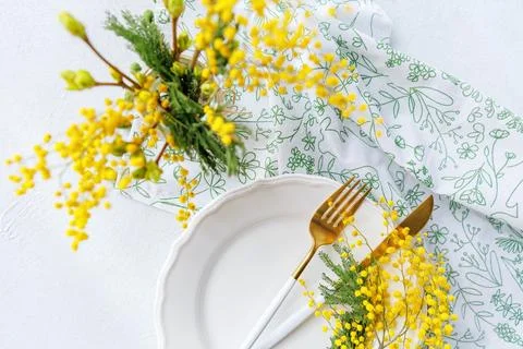 Bright spring table setting with mimosa flowers and golden flatware Stock Photos