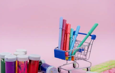 Bright stationery objects in mini supermarket cart on pink background. Back t Stock Photos