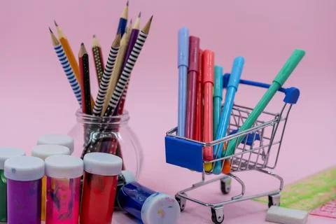 Bright stationery objects in mini supermarket cart on pink background. Back t Stock Photos