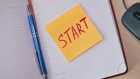 A bright sticky note with the word START is placed on an open notepad beside a Stock Footage 339094150