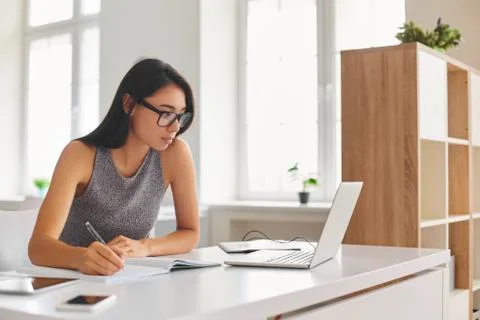 Bright student taking notes in notebook and using laptop computer for e-learning Stock Photos