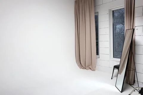 Bright studio with large windows, beige curtains and mirror near wall. Stock Photos