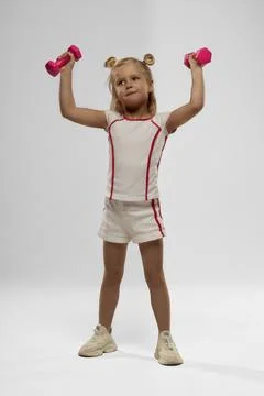 Bright studio setting featuring a small blonde girl exercising with dumbbells Stock Photos