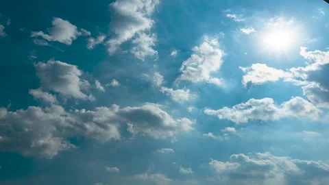 Bright summer sun shining through white fluffy clouds in a clear blue sky Stock Footage 342332192
