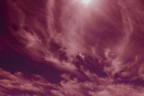 Bright sun above wispy clouds in a pink tinted sky. Stock Photos
