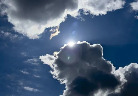 Bright sun behind dramatic clouds in a deep blue sky. Backlit cumulus forms.. Stock Photos