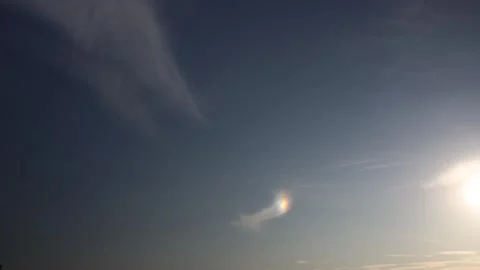 Bright sun in clear sky with rare rainbow-colored sundog glowing beside wispy cl Stock Footage 312604380