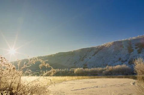 Bright sun in the cloudless sky. Freezing river from the hilly banks and larg Stock Photos
