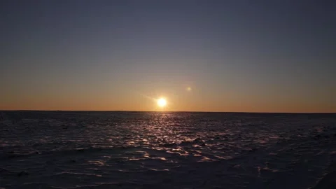 Bright sun on dark blue sky setting over snow field at sunset Stock Footage 303336629