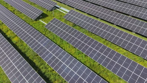 Bright sun glare reflects off angled solar panel rows, narrow grass strips Stock Footage 346174509