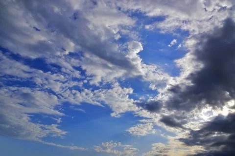 The bright sun hid behind light white clouds in the blue sky. Great backgroun Stock Photos