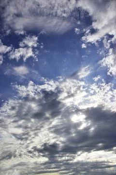 The bright sun hid behind light white clouds in the blue sky. Great backgroun Stock Photos