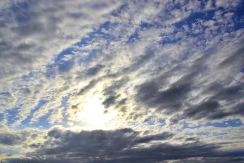 The bright sun hid behind light white clouds in the blue sky. Great backgroun Stock Photos