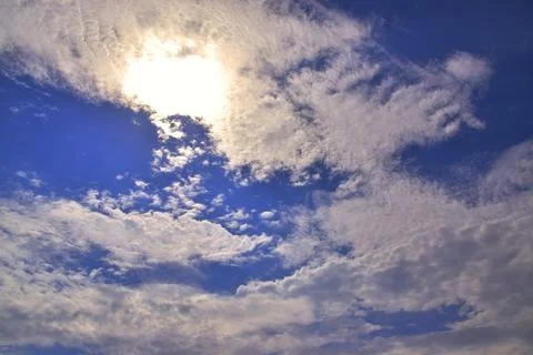 The bright sun hid behind light white clouds in the blue sky. Great backgroun Stock Photos