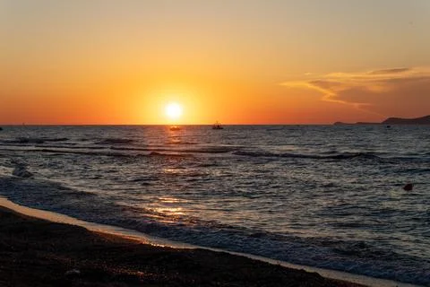 Bright sun low over dark ocean waves near beach shore at sunset Fotos Stock