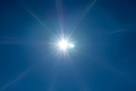 Bright sun with rays shining in a clear blue sky. Stock Photos