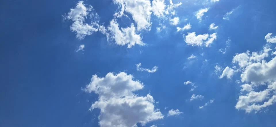 Bright sun rays shining through fluffy white clouds on a deep blue sky Stock Photos