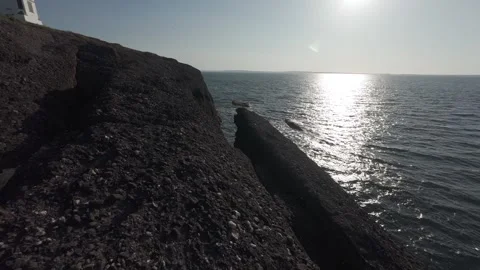 Bright sun reflections on calm ocean water beside dark coastal rocks Stock Footage 340462409