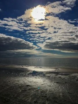 Bright sun reflects on calm ocean water under clouds near the beach during .. Stock Photos