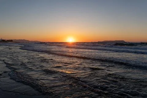 Bright sun setting on horizon over wavy ocean water at dusk Photos