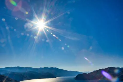 Bright sun shines on cloudless blue sky over beautiful lake in mountain valley Stock Photos