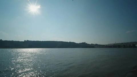 Bright sun shines high above a wide river with a bridge Stock Footage 339630042
