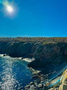 A bright sun is shining down on a rocky coastline. The water reflects light,  Stock Photos