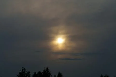 Bright sun shining through dark dramatic clouds over tree silhouettes Foto stock