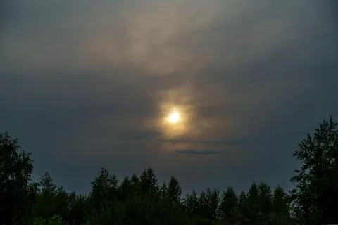 Bright sun shining through dark dramatic clouds over tree silhouettes Foto stock