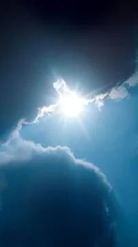 Bright sun shining through dark, dramatic clouds in a clear blue sky, creat.. Stock Photos