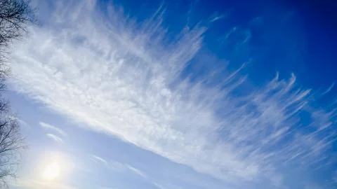 Bright sun shining through delicate white cirrus clouds in a deep blue sky .. Stock Photos