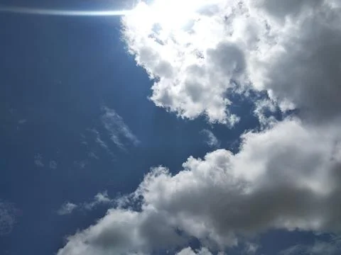 Bright sun shining through fluffy white clouds in blue sky with sunlight Stock-Fotos