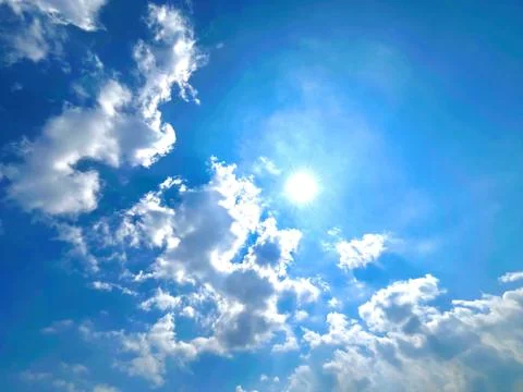 Bright Sun Shining Through Fluffy White Cumulus Clouds in Clear Blue Sky Stock Photos