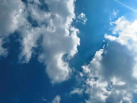 Bright Sun Shining Through Fluffy White Cumulus Clouds in Clear Blue Sky Stock Photos