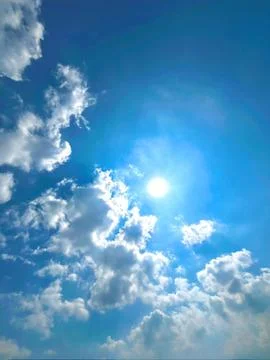 Bright Sun Shining Through Fluffy White Cumulus Clouds in Clear Blue Sky Foto stock