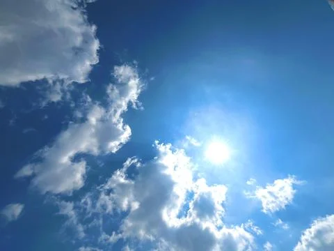 Bright Sun Shining Through Fluffy White Cumulus Clouds in Clear Blue Sky Stock Photos